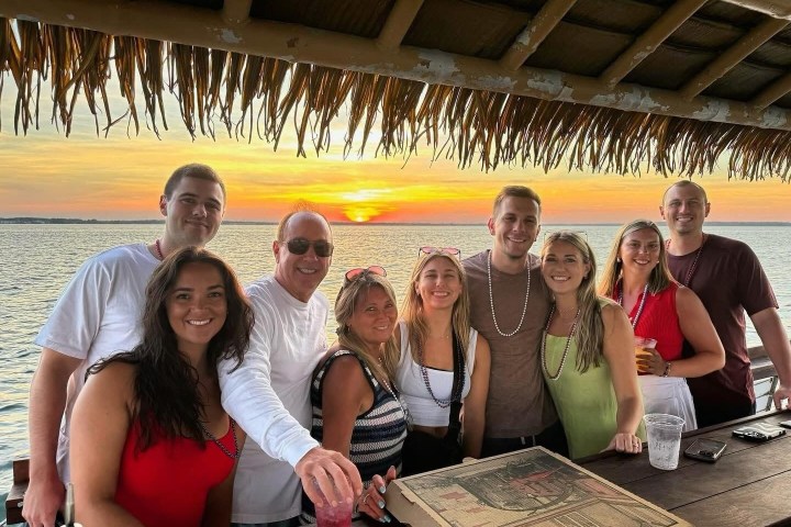 Group of people smiling at a beach bar during sunset.