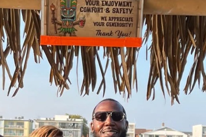 Group of five smiling people under a tiki hut roof with a 'Tip the Crew' sign above.