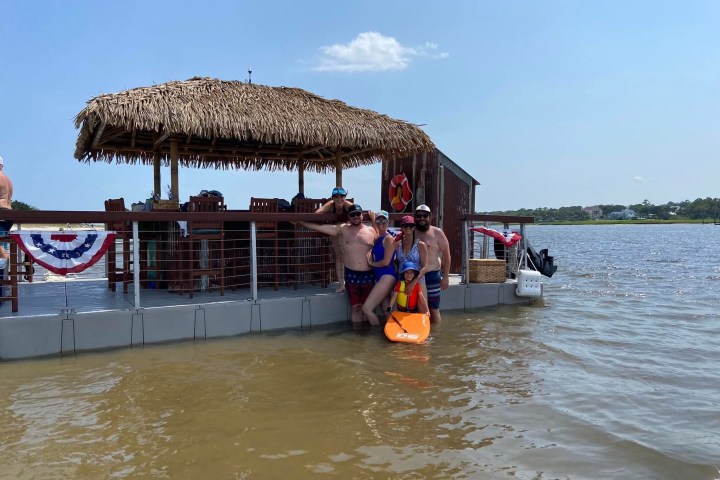 People in swimsuits relaxing on a floating tiki bar in a lake.