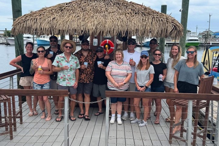 Group of people posing on a dock under a thatched roof with boats in the background.