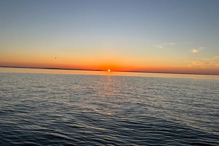 Sun setting over calm ocean waters with a clear sky.