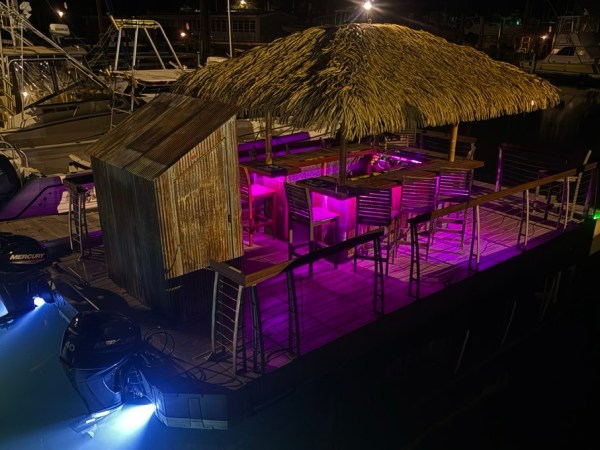 Floating tiki bar with thatched roof lit by colorful lights at night.