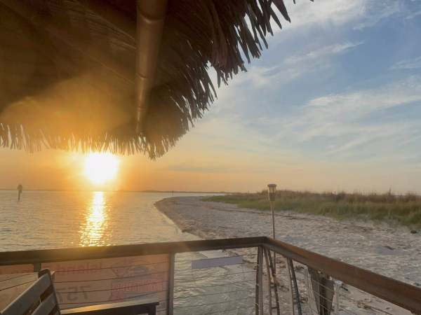 Sunset view from a beach hut with a sandy shoreline and calm sea.