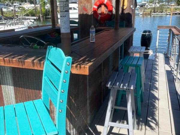 Outdoor tiki bar by water with turquoise chairs and wooden accents.