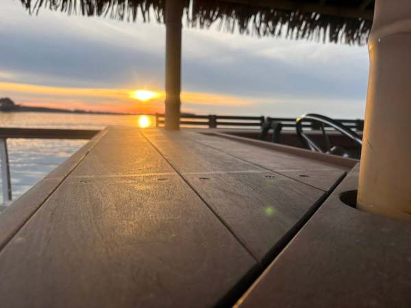 Sunset view from under a thatched roof hut by the water.