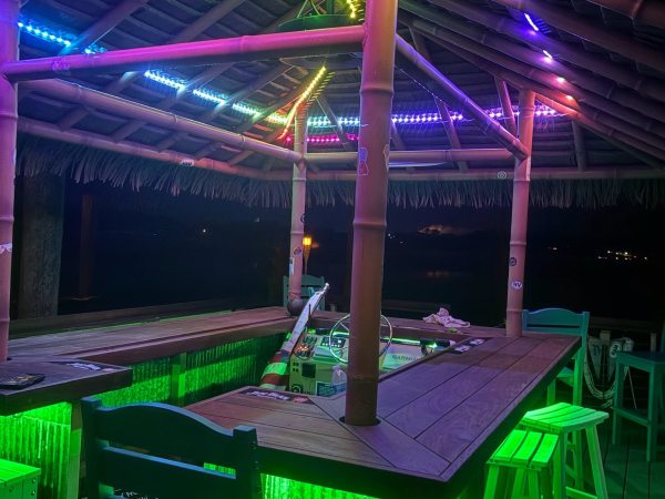 Tiki bar with colorful LED lights under a thatched roof at night.