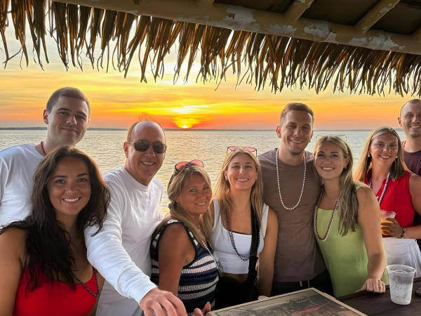 Group of nine people smiling at a beachside bar during sunset.