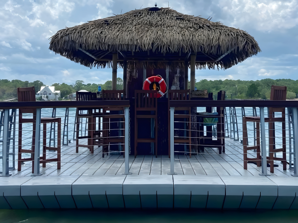 Floating tiki bar on a lake with a thatched roof and chairs.