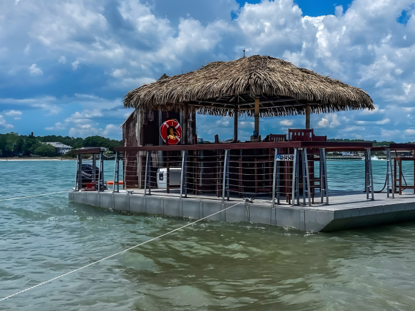 Floating tiki bar on a lake with cloudy sky.