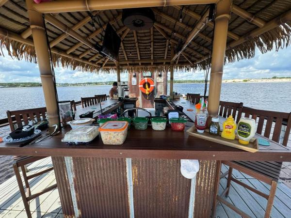Tiki bar on a dock with food spread and water in the background.
